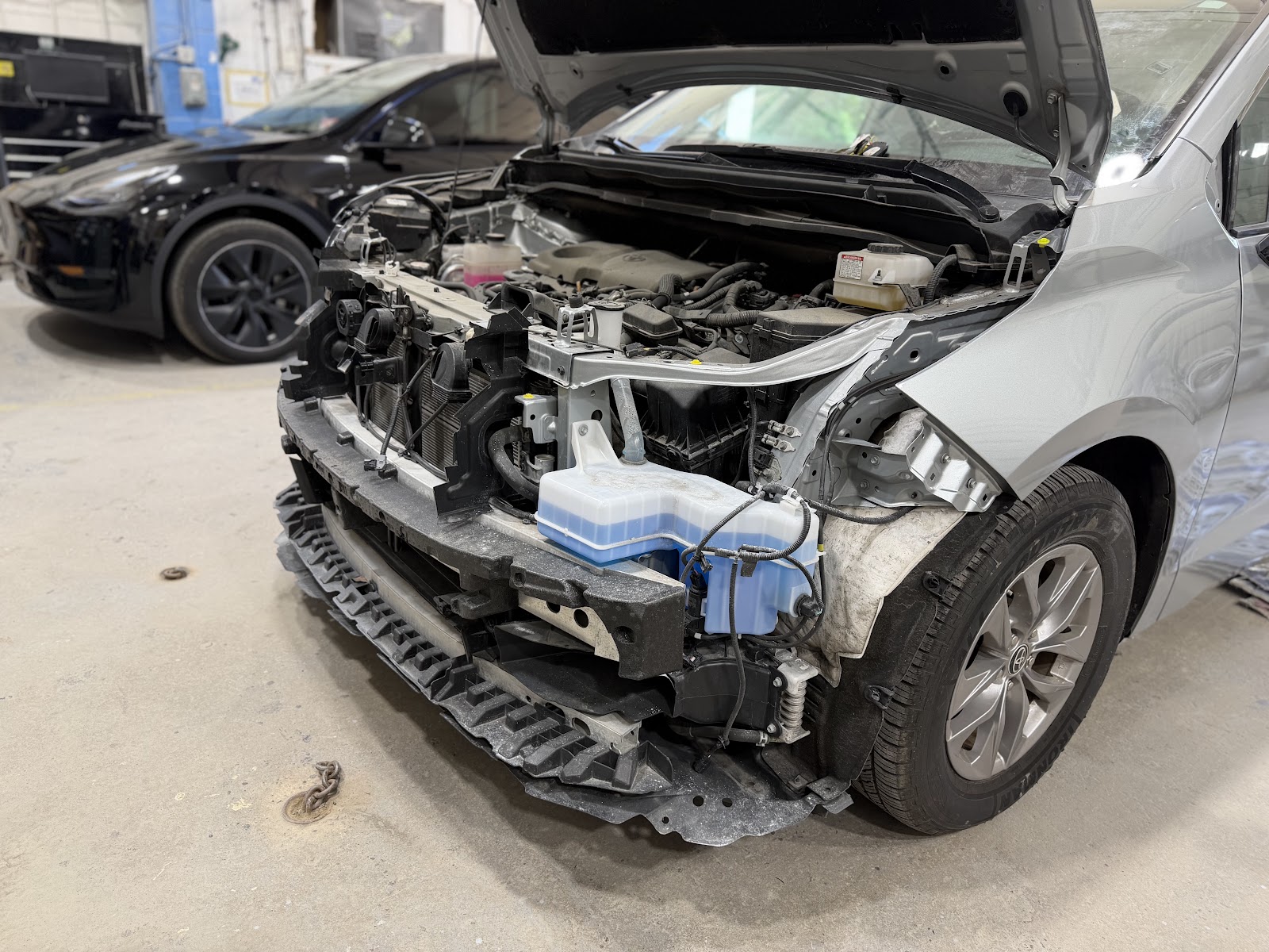 Silver minivan with its front bumper removed inside Yitz's shop